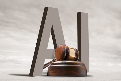 A gavel sits in front of the letters, AI, which illustrates the legal ramification and questions surrounding the implementation of artificial technologies.