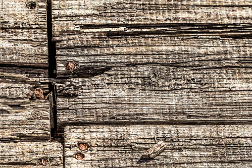 Old, weathered, rotten, cracked, knotted Pine wood planks, fixed with eroded rusty external hexagon flange bolts.