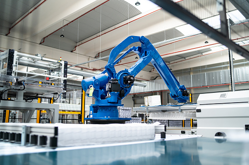 A heavy industrial robotic arm is working as part of a conveyor belt automated factory in a manufacturing plant