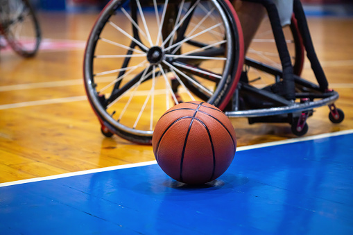Basketball sitting on the wooden flooring of indoor basketball court next to professional customizable basketball wheelchair