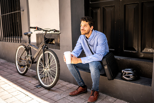 Young man with bicycle relaxing with a coffee cup looking away outdoors