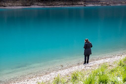 Woman in black clothes standing on lakeside of Auronzo Lake, in Auronzo di Cadore village; Beautiful turquoise water; Belluno, Dolomites, Italy