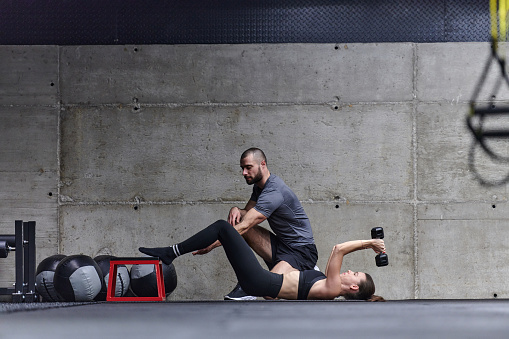 A muscular man assisting a fit woman in a modern gym as they engage in various body exercises and muscle stretches, showcasing their dedication to fitness and benefiting from teamwork and support.