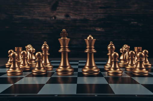 Leader and competition. White Chess King among lying down black pawns on chessboard, dark blue background.