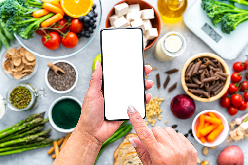Woman holding smartphone with white screen mock-up on healthy vegan food background