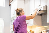 A woman is cleaning a stove hood surface in a kitchen
