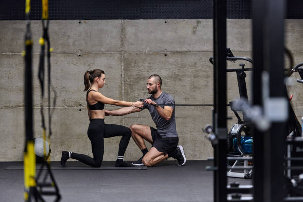 A muscular man assisting a fit woman in a modern gym as they engage in various body exercises and muscle stretches, showcasing their dedication to fitness and benefiting from teamwork and support. un hombre musculoso que ayuda a una mujer en forma en un gimnasio moderno mientras participan en varios ejercicios corporales y estiramientos musculares, mostrando su dedicación al acondicionamiento físico y beneficiándose del trabajo en equipo y el apo