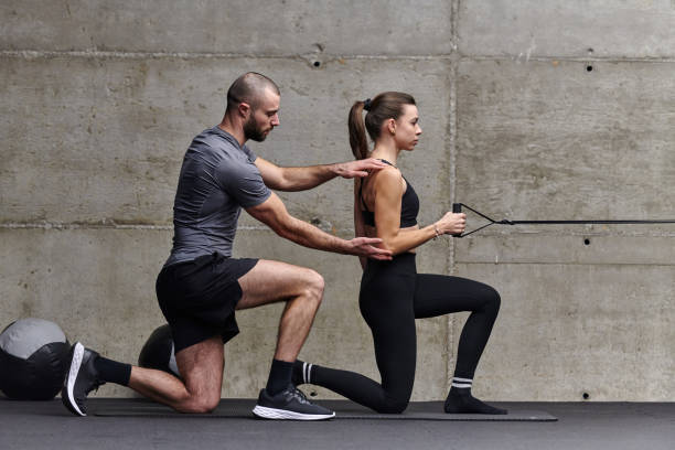 A muscular man assisting a fit woman in a modern gym as they engage in various body exercises and muscle stretches, showcasing their dedication to fitness and benefiting from teamwork and support. un hombre musculoso que ayuda a una mujer en forma en un gimnasio moderno mientras participan en varios ejercicios corporales y estiramientos musculares, mostrando su dedicación al acondicionamiento físico y beneficiándose del trabajo en equipo y el apo