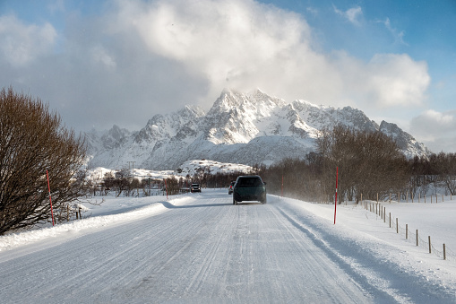 Car driving on snow covered road with mountain in countryside at Lofoten Island, Norway