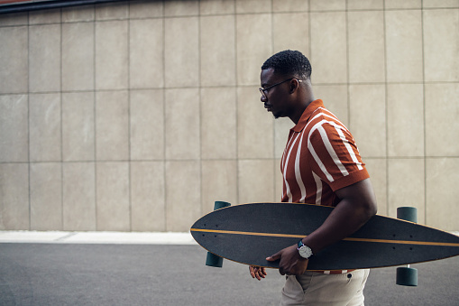 Side view of young man carrying a longboard and walking