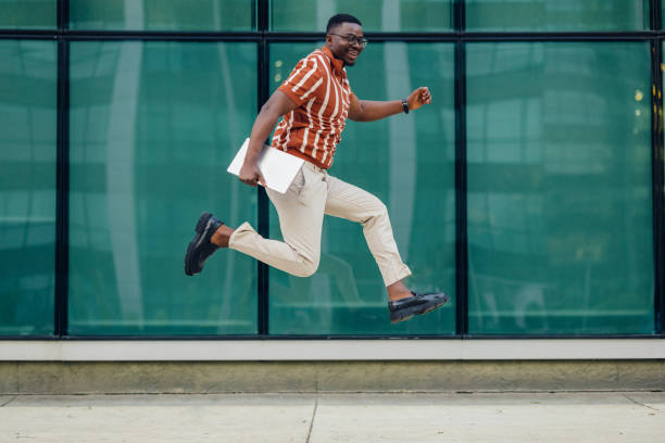 Happy young businessman jumping with laptop