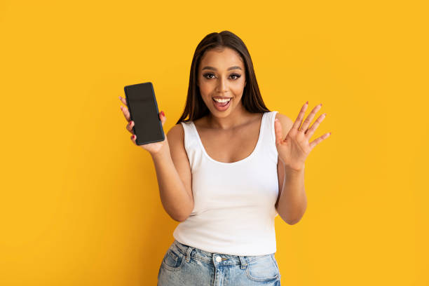 istock Young happy woman wearing basic clothes smiling to the camera and showing cellphone screen, posing over yellow studio background. 1492677154