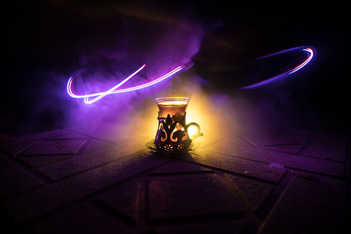 Arabian tea in glass with eastern snacks on a stone surface on dark background with lights and smoke. Eastern tea concept. Selective focus.