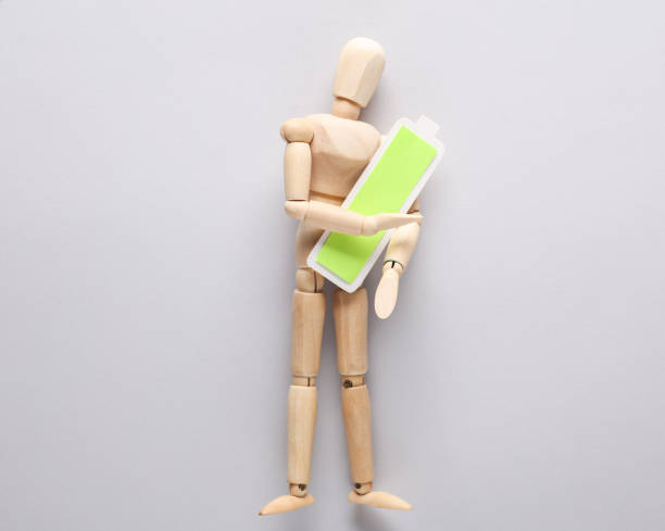 istock Wooden puppet holding a fully charged battery on a gray background 1492682465