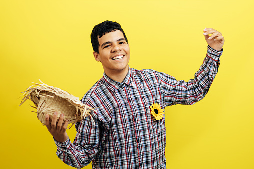Brazilian teenager boy wearing typical clothes for the Festa Junina dancing on color background