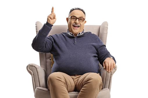 Happy mature man sitting in an armchair and pointing up isolated on white background