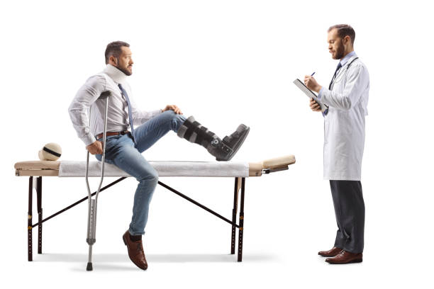 man with an orthopedic boot and neck collar sitting on a therapy table and physical therapist writing a document - physical injury men orthopedic equipment isolated on white imagens e fotografias de stock
