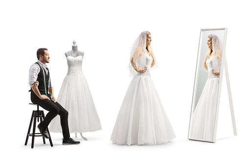 Bride trying on a dress at the tailors workshop and looking at a mirror isolated on white background