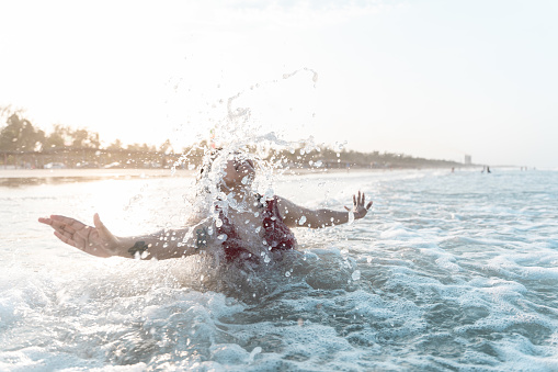 A young Hispanic woman is playing with the waves being splashed by the sea in her face during summer vacation