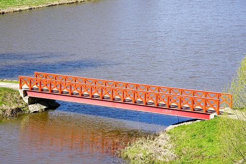 A small beautiful orange pedestrian bridge over a river with a steel girder base and wooden railings, simple straight footbridge