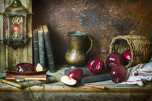 Classic still life with fresh red apples placed with antique jar and old books on rustic wooden background.