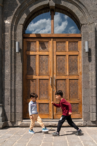 image of brothers playing in front of historic stone house.Historic house made of wooden door and volcanic stone. brothers spending time together in street. Shot with a full-frame camera in daylight.