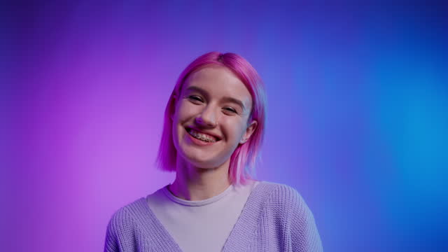 Positive young woman with pink hair and braces laughing on gradient background