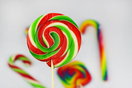 Colorful round lollipop, bright sweet candy in white, red and green colors. Christmas or New year lollipop on white background with other multicolored lollipops blurred behind. Close up