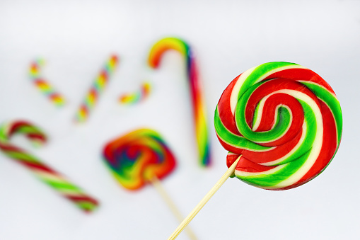 Colorful round lollipop, bright sweet candy in white, red and green colors. Christmas or New year lollipop on white background with other multicolored lollipops blurred behind. Close up