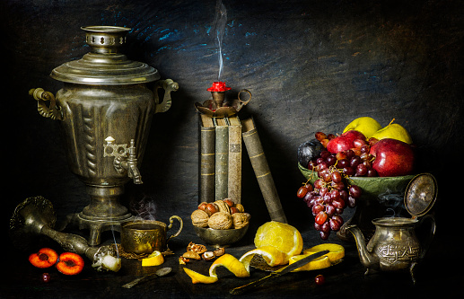 Classic still life with vintage books placed with old silver samovar, candlesticks, fresh fruits, cup of tea, tea pot and nuts on vintage background.