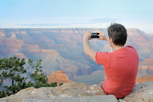 Middle age male tourist making mobile photo of the famous Grand Canyon from Mather Point. Handsome man traveling, having fun and admiring sightseeing of usa.