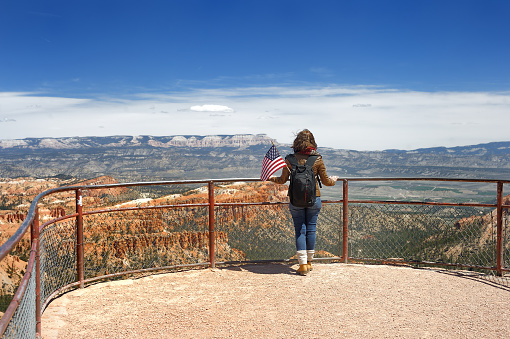 Young woman tourist with american flag admiring of amazing view of Bryce Canyon National Park, Utah, United States