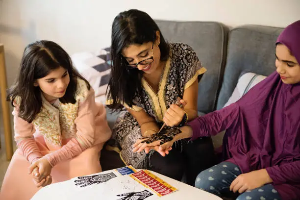 North-American muslim woman and girls drawing with henna at Ramadan. Childs are preteen, oldest girl is wearing a hijab. Traditional Lebanese and Moroccan dress. Horizontal waist up indoors shot. This was taken in Quebec, Canada.