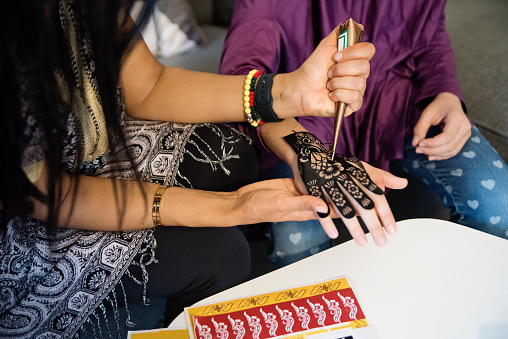 North-American muslim woman and girls drawing with henna at Ramadan. No faces. Traditional Lebanese and Moroccan dress. Horizontal waist up indoors shot. This was taken in Quebec, Canada.