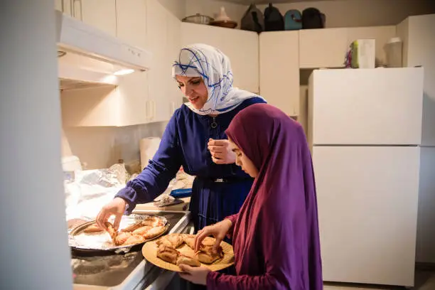 North-American muslim mother and daughter preparing Iftar at Ramadan. They are wearing an hijab and girl is helping her mother to prepare traditional middle-eastern food. Horizontal waist up indoors shot with copy space. This was taken in Quebec, Canada.