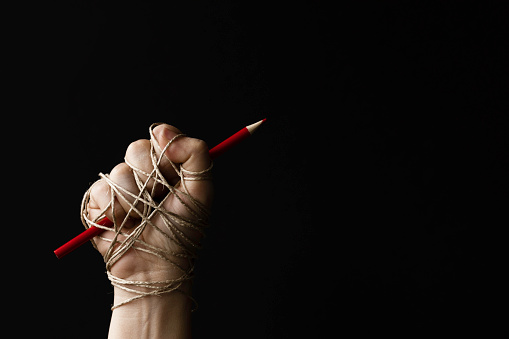 Hand holding red pencil and is tied up with rope. Representing freedom speech, freedom of expression issues.