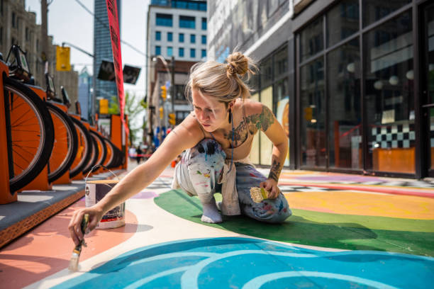 Young Caucasian woman artist painting sidewalk mural stock photo