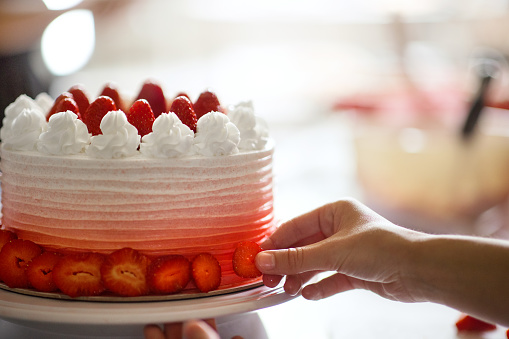Closeup of an unrecognizable woman putting icing on a strawberry cake at a small family owned cake shop.