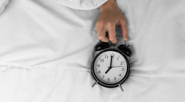 istock Woman's hand holding black alarm clock on bed 1492719576