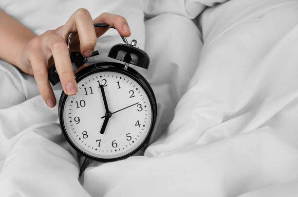 istock Woman's hand turning off black alarm clock on bed 1492719587