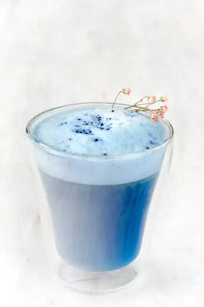 Photo of Blue matcha latte in a glass on a light white table.