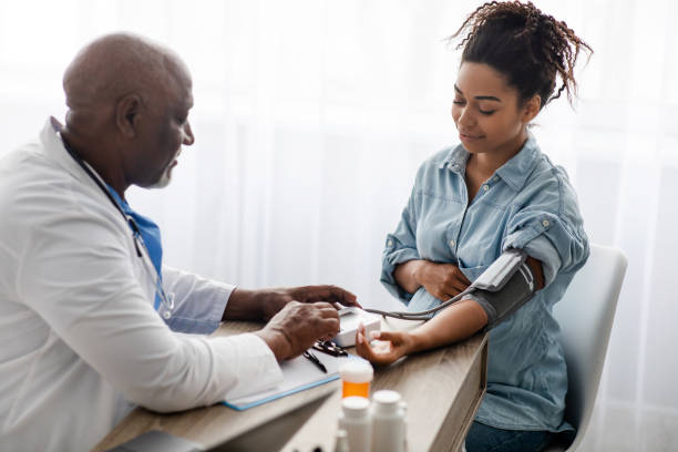 Black doctor checking measuring pressure of pregnant patient stock photo