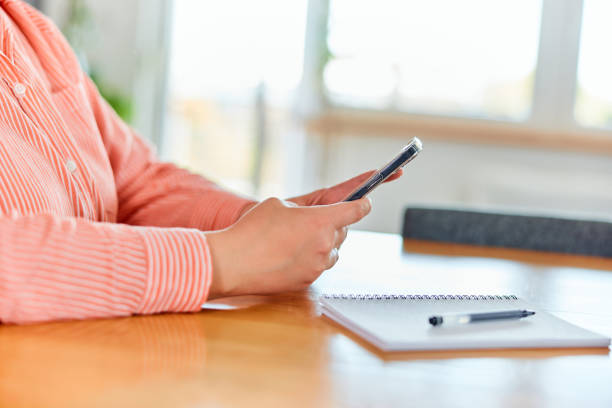 istock A close-up of a female's hands, using a mobile phone, having a notebook on the table. 1492726404