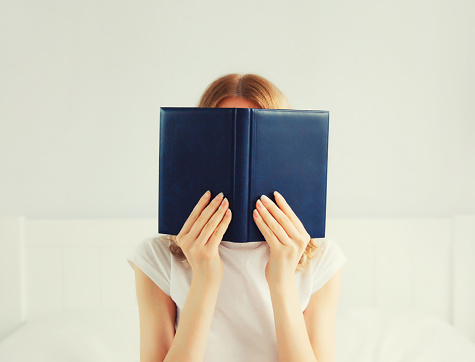 Young sad tired woman student covering her face with open book with blank cover