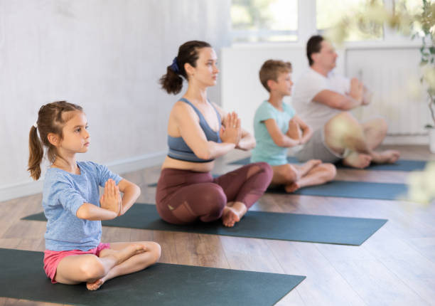 angenehmes kleines mädchen, das mit ihrer familie lotushaltung von yoga praktiziert - yoga good posture women little girls stock-fotos und bilder