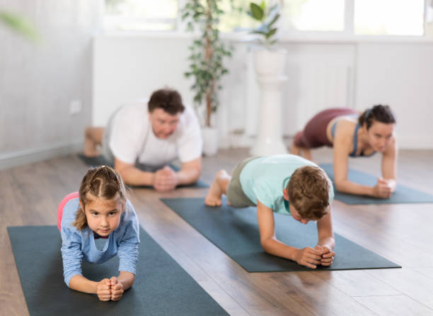 angenehmes kleines mädchen, das mit ihrer familie die plank-pose des yoga praktiziert - yoga good posture women little girls stock-fotos und bilder