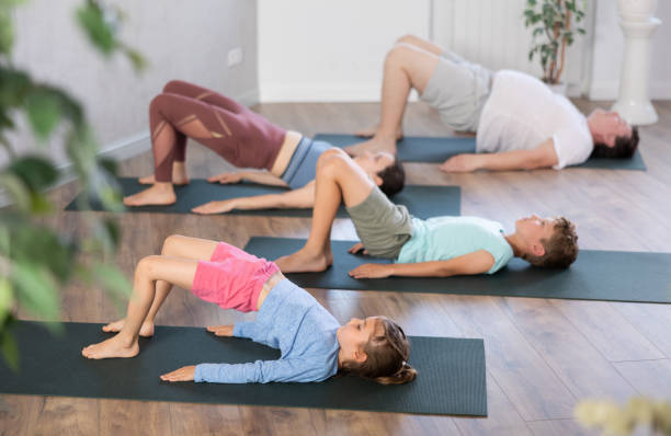 fleißiges kleines mädchen, das mit ihrer familie die bridge-pose des yoga praktiziert - yoga good posture women little girls stock-fotos und bilder