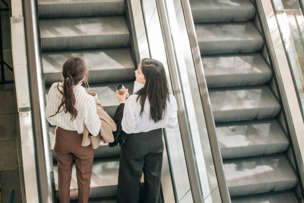 istock Two Asian women talking on escalator on way to work 1492749428