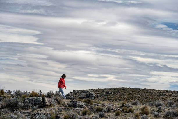 Senior woman walks through the field with lenticular clouds in the background in Puerto Deseado, Santa Cruz, Argentina.