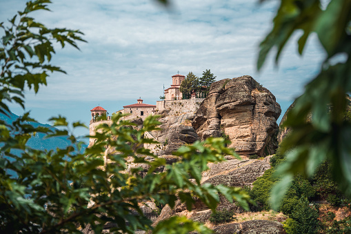 A view through the leaves of a stone building on top of a giant rocky formation, popular tourist spot.